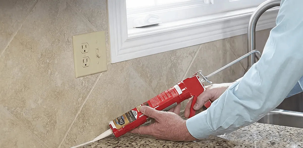 Handyman applying caulk along a kitchen backsplash and countertop seam in Nashua, NH