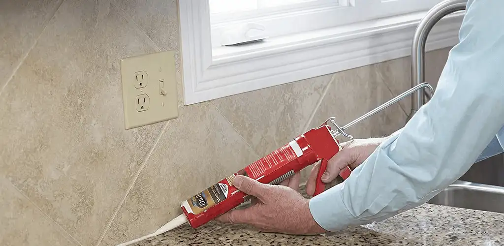 Handyman applying caulk along a kitchen backsplash and countertop seam in Nashua, NH