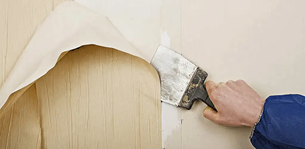 Handyman removing wallpaper with a scraper for wall preparation in Nashua, NH