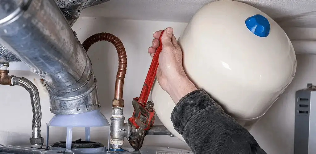 Water heater repair technician tightening plumbing connections near a tank unit in Nashua, NH